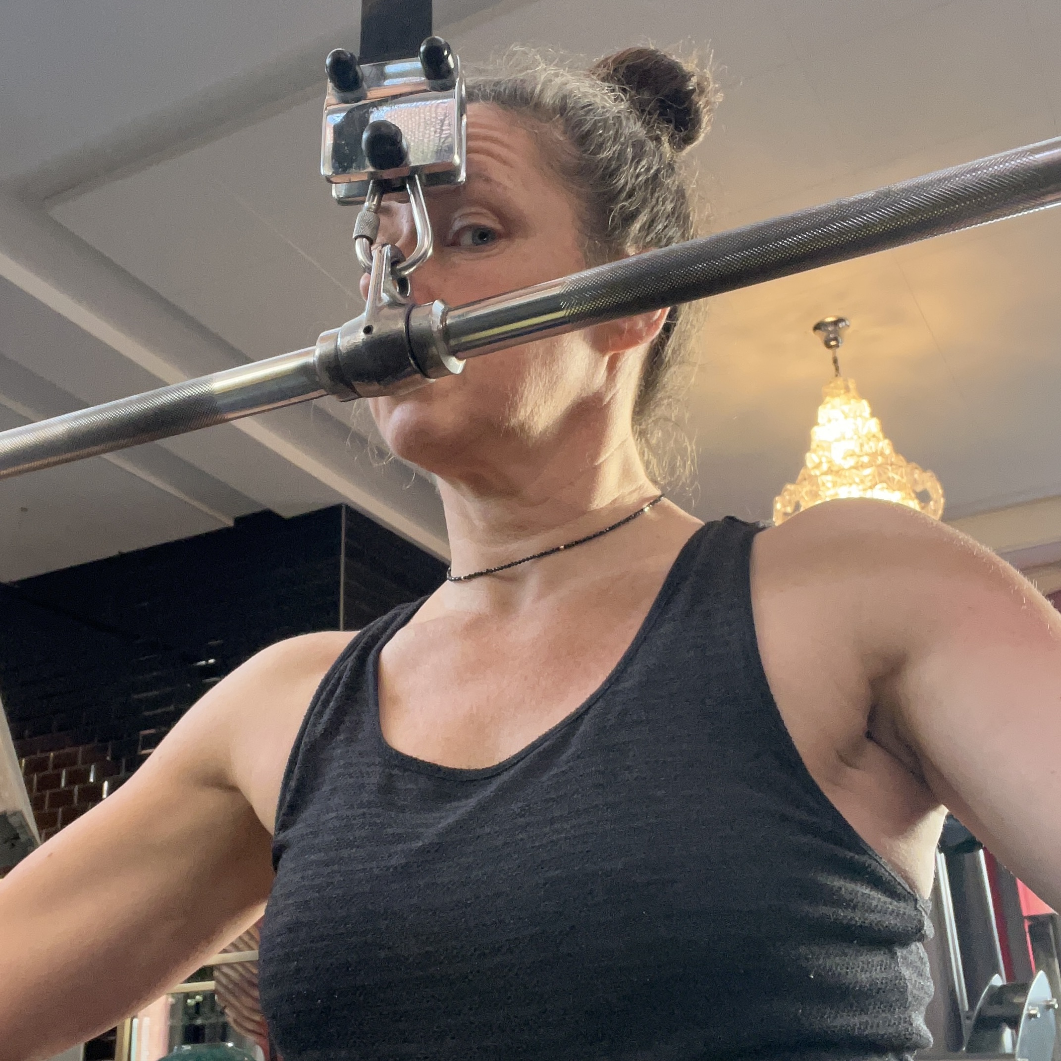 Eine Frau in einem Tanktop hält eine Gewichtsbar mit einem Kinnhalter in einem Fitnessstudio.