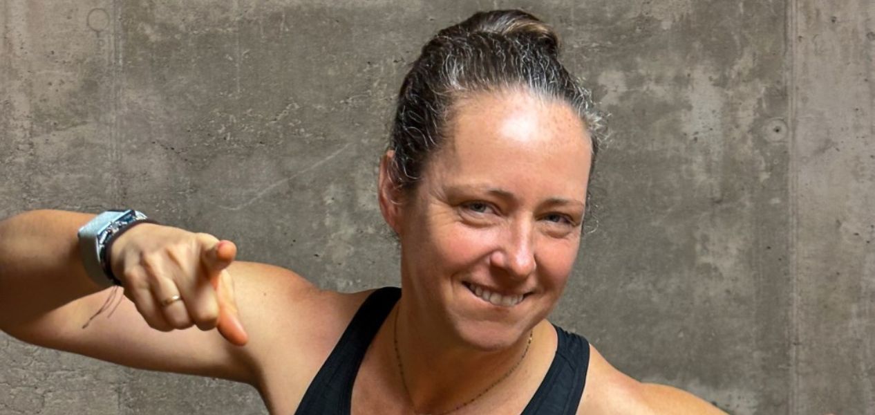 Eine lächelnde Frau zeigt mit dem Daumen nach oben, während sie ein Sportoutfit trägt.