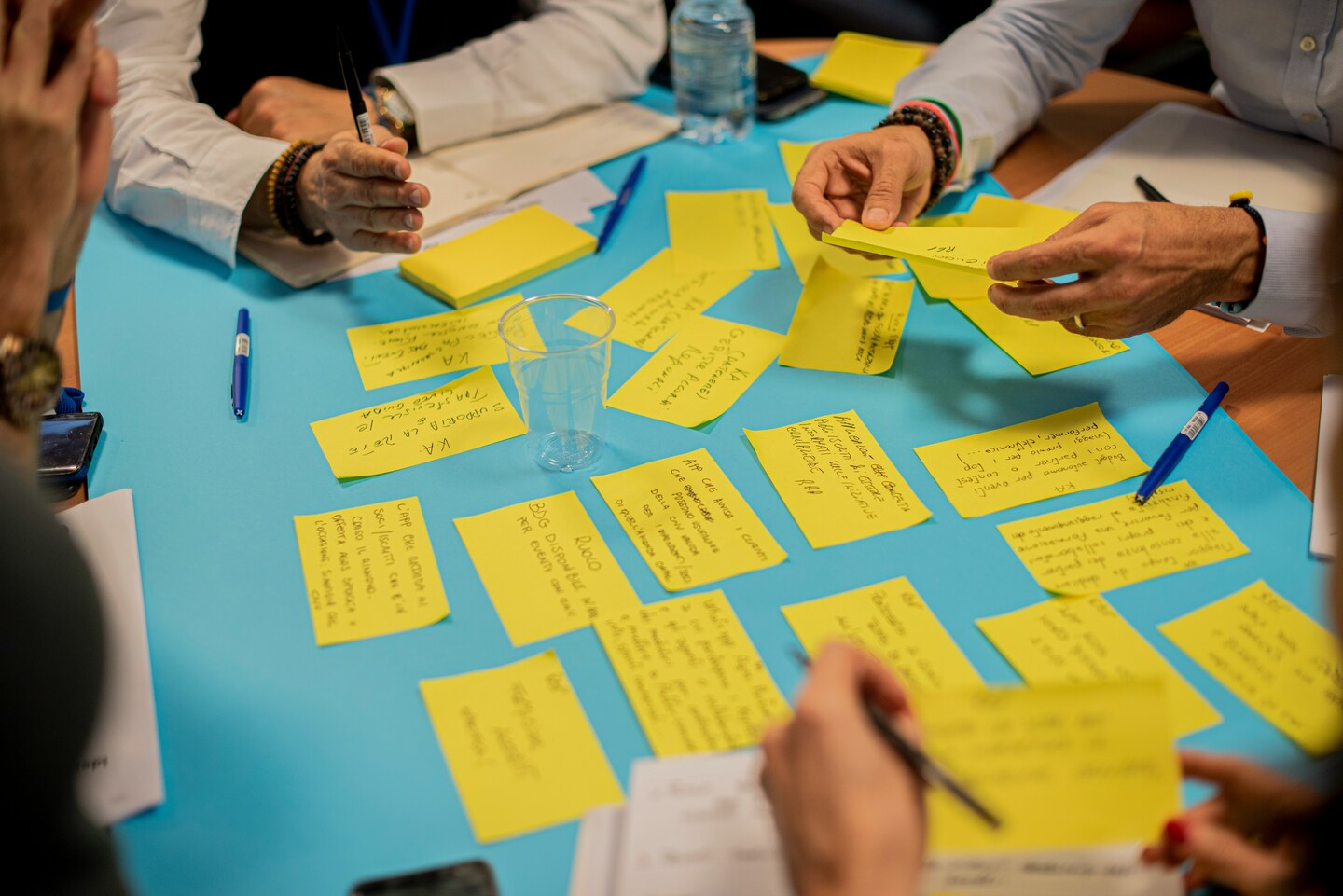 Mehrere Personen arbeiten an einem Tisch mit gelben Post-its, Notizen und Stiften.