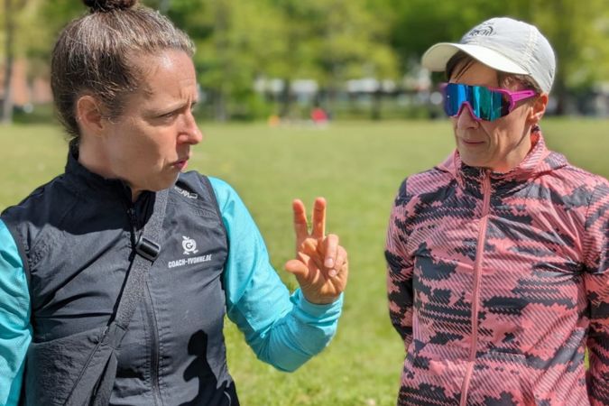 Zwei Frauen stehen im Freien und unterhalten sich, eine zeigt mit dem Finger eine Geste.